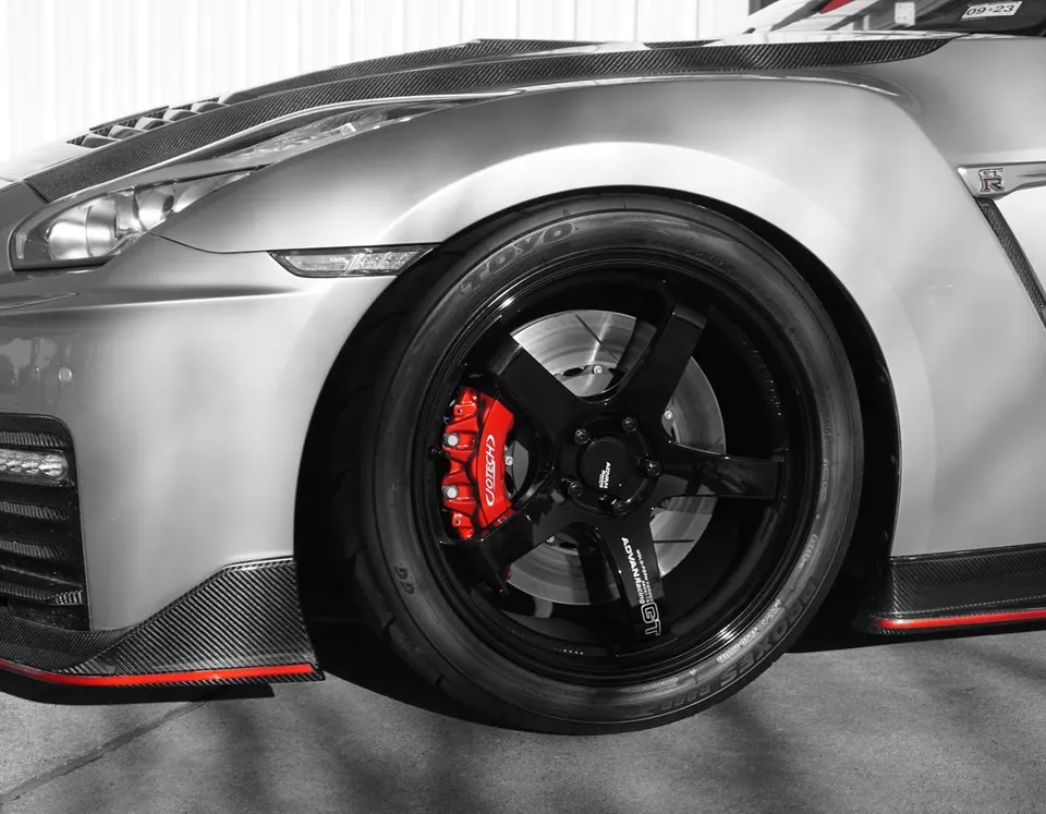 Close-up of a silver Nissan GT-R's front wheel, featuring black Advan wheels, red Jotech calipers, and carbon fiber aero.
