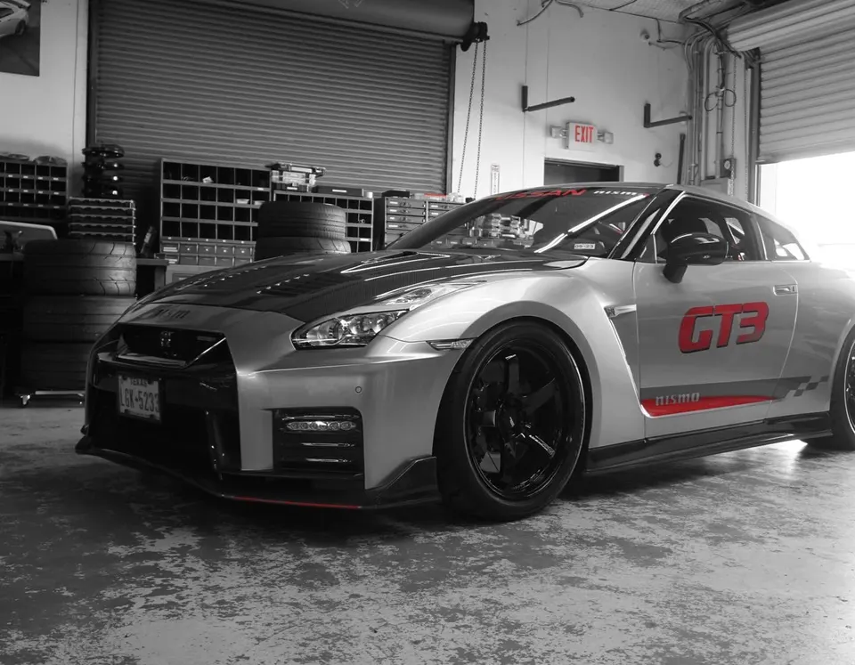 A silver Nissan GT-R R35 with a carbon fiber hood and GT3 livery parked inside a performance shop.