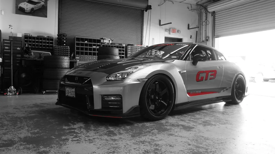 Silver Nissan GT-R with GT3 livery and custom black wheels parked in a performance tuning shop.