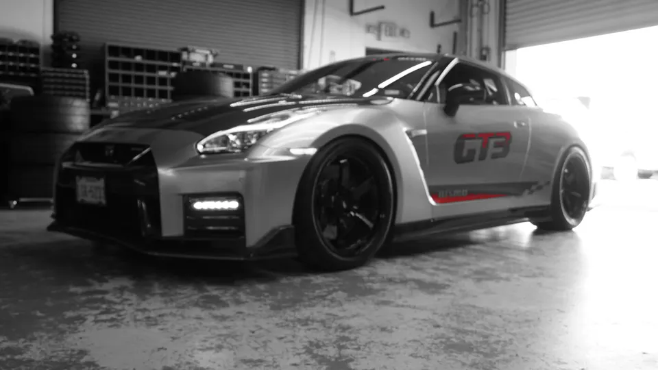 Silver Nissan GT-R R35 with GT3 livery and custom black wheels parked inside a performance shop.
