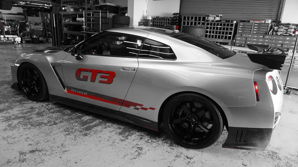 Silver Nissan GT-R with GT3 livery and aftermarket wheels parked inside a performance tuning shop.