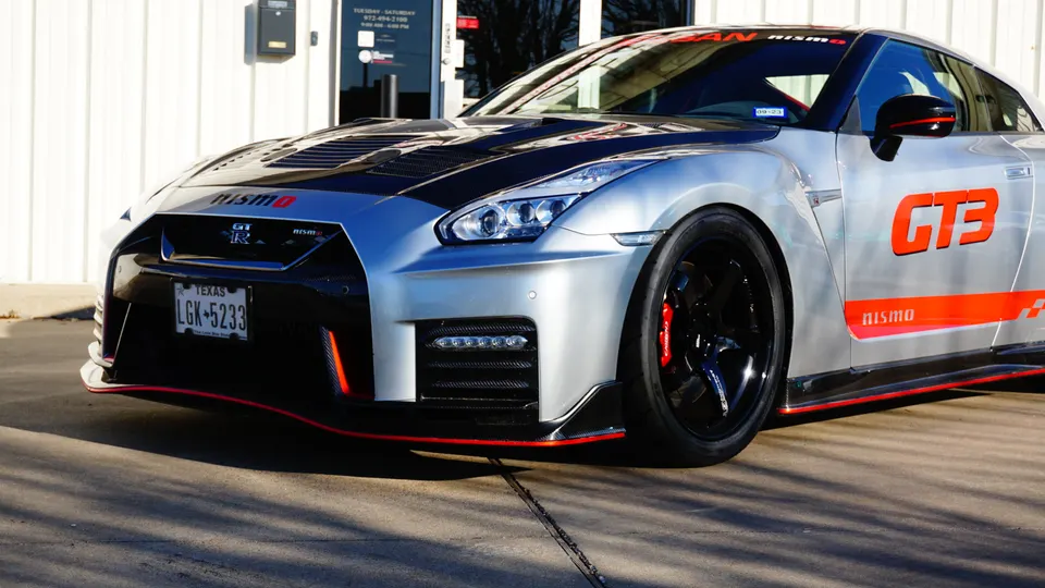 Silver Nissan GT-R Nismo GT3 with carbon fiber aero and red accents parked outside a building.