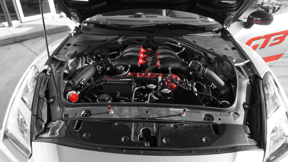 A detailed view of a Nissan GT-R R35 engine bay featuring a red carbon fiber intake manifold and performance air intakes.