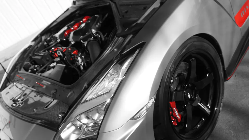 Close-up of a Nissan GT-R's open engine bay with red intake manifolds and black wheels with red brake calipers.