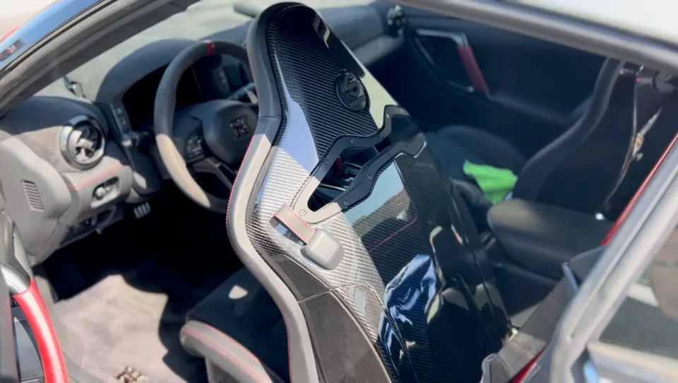 Close-up of a Nissan GT-R interior featuring a carbon fiber racing seat and alcantara steering wheel.