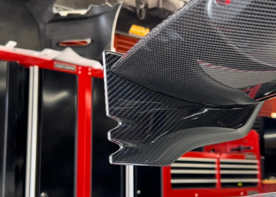 A close-up of a carbon fiber aerodynamic part, possibly a wing endplate or diffuser, in a performance shop.