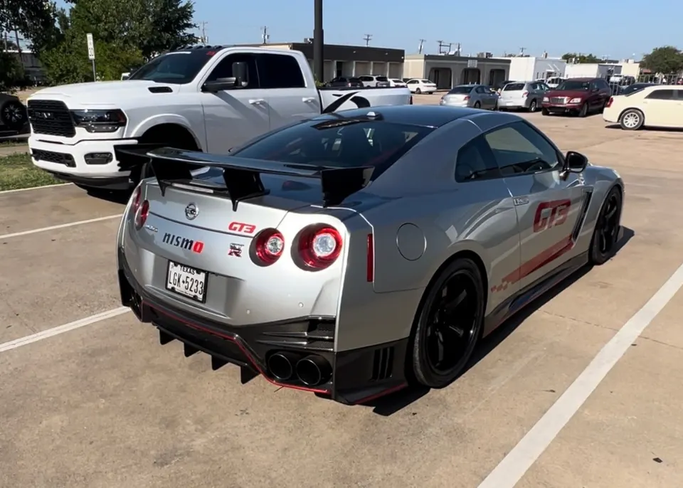 A silver Nissan GT-R Nismo with a large rear wing and diffuser parked in a lot on a sunny day.