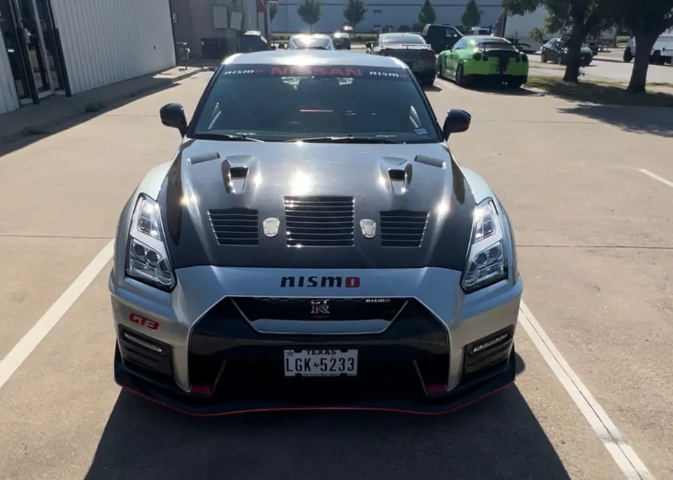 Front view of a silver Nissan GT-R R35 with a carbon fiber hood and Nismo badging parked outdoors.