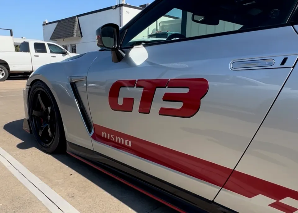 Silver Nissan GT-R with red GT3 and Nismo decals on the side, featuring black aftermarket wheels.