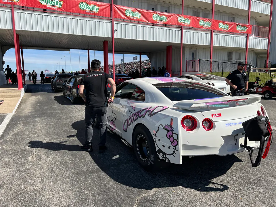 White Nissan GT-R with Hello Kitty livery in the staging lanes at a drag strip, with a Jotech crew member.