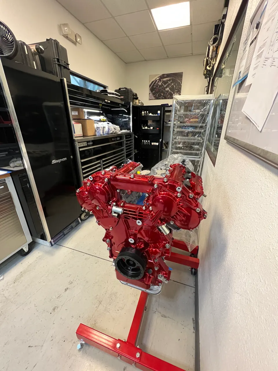A vibrant red built engine mounted on an engine stand in a performance tuning shop, surrounded by tools and equipment.