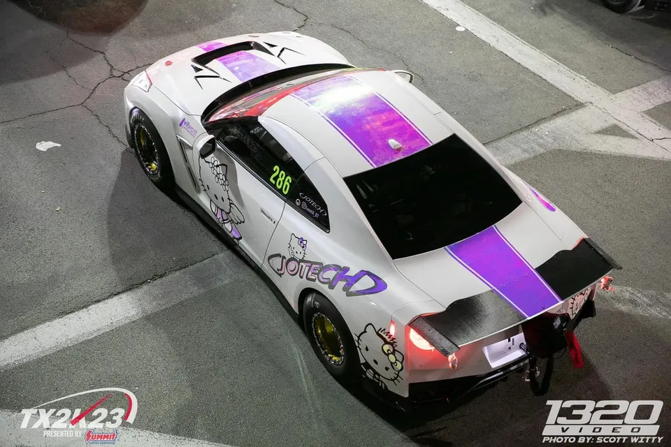 Overhead view of a white Nissan GT-R drag car with purple stripes and Hello Kitty decals at a track event.