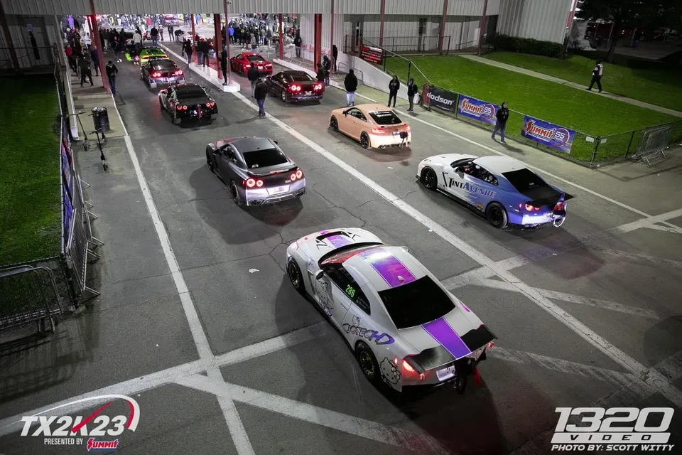 Multiple Nissan GT-Rs lined up in the staging lanes at a night drag racing event, with spectators watching.
