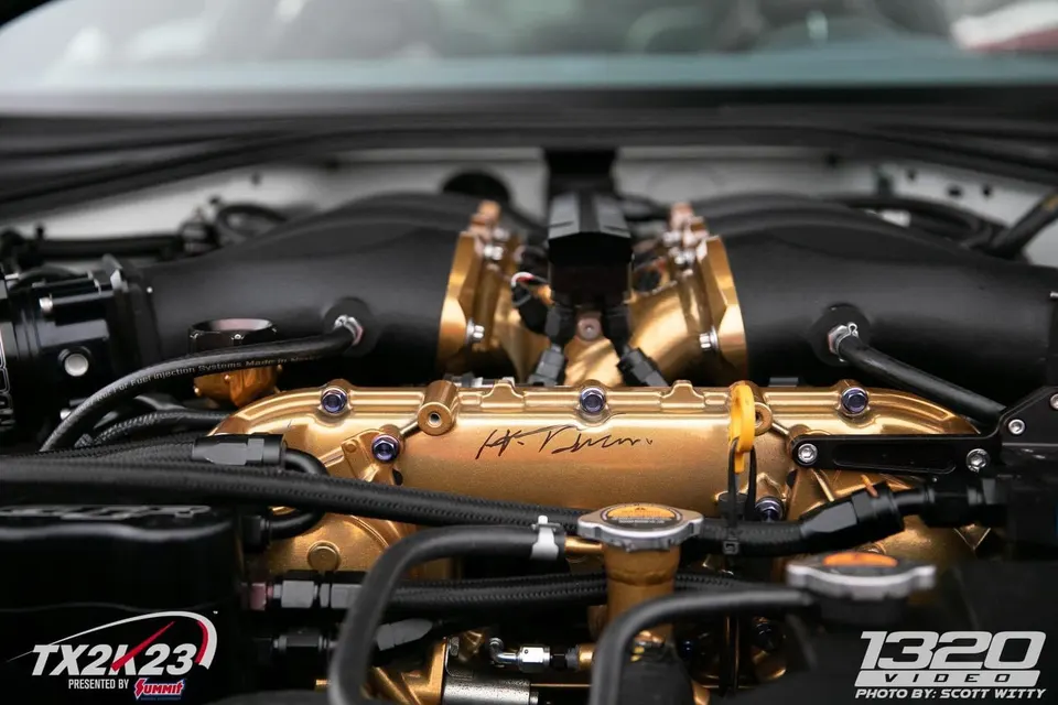 A close-up of a custom gold and black performance engine bay featuring an aftermarket intake manifold and fuel rails.