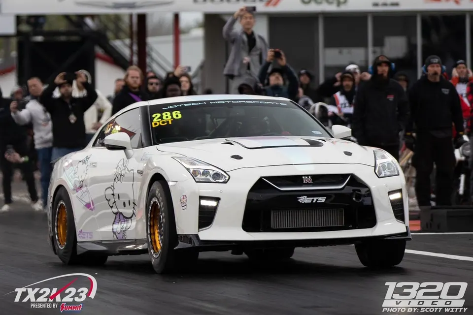 A white Nissan GT-R with Hello Kitty livery on a drag strip at TX2K23, ready to race.