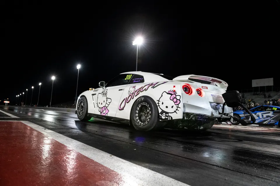A white Nissan GT-R drag car with Hello Kitty decals on a drag strip at night, ready to race.