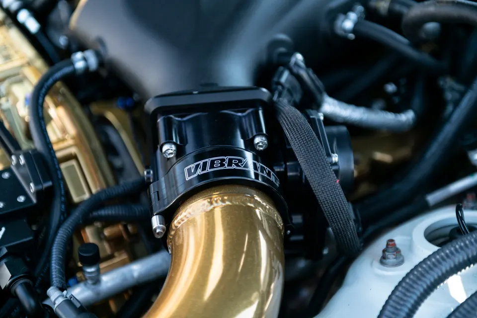 Close-up of a Vibrant Performance clamp on a gold boost pipe in a high-performance car engine bay.