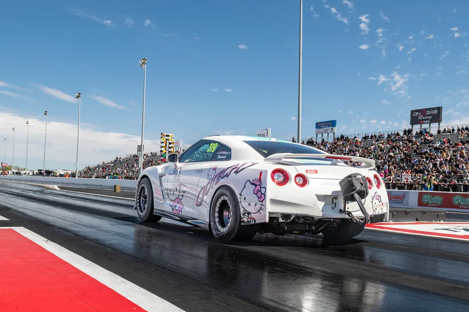 White Nissan GT-R with Hello Kitty livery launching on a drag strip, showing drag wheels and a parachute.