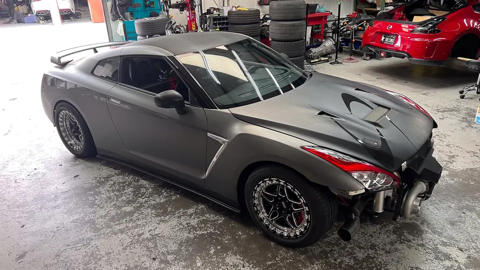Matte grey Nissan GT-R with front bumper removed, showcasing large twin turbos and custom exhaust in a performance shop.