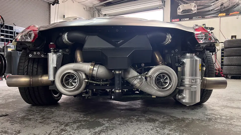 A Nissan 350Z with a custom twin-turbo setup and exposed exhaust in a performance tuning shop.