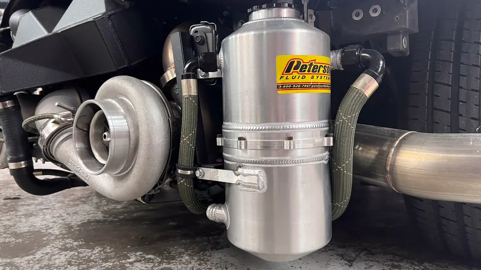 Close-up of a turbocharger, Peterson Fluid Systems tank, and exhaust pipe on a high-performance vehicle.