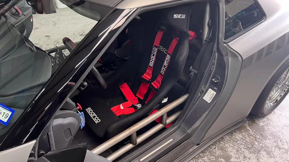 Interior of a modified Nissan GT-R featuring a Sparco racing seat, red harnesses, and a custom roll cage.
