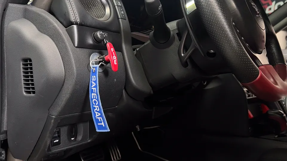 Close-up of a car's interior showing the steering wheel, ignition with a Safecraft keychain, and dashboard.