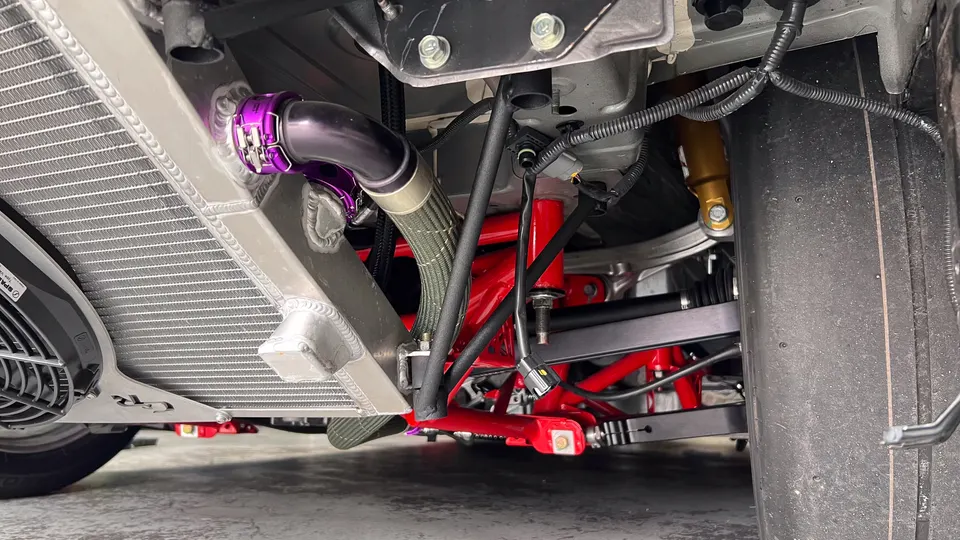 Close-up view of a performance car's undercarriage showing an aluminum radiator, red suspension components, and purple piping.