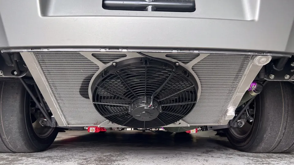 Close-up view of a custom rear-mounted radiator and cooling fan system on a high-performance car, with drag slicks visible.