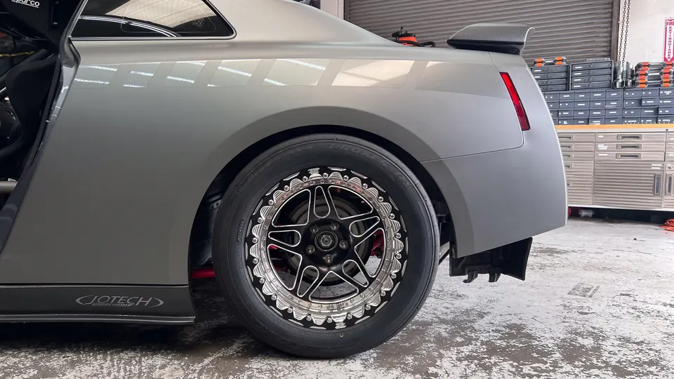 Rear view of a grey Nissan GT-R with drag wheels and slick tires in a Jotech Motorsports shop, showing interior safety features.
