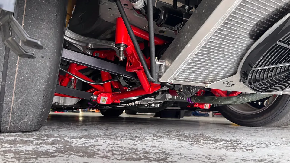 Close-up view of a car's underbody, showcasing red aftermarket suspension components, a large radiator, and a wide drag tire.