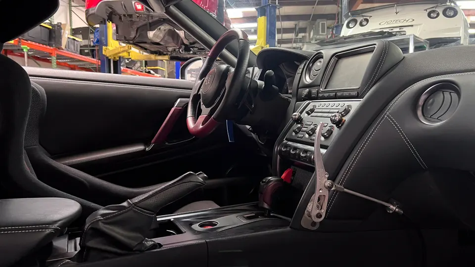 Interior of a Nissan GT-R in a performance shop, showcasing a custom shifter, race seat, and dashboard.