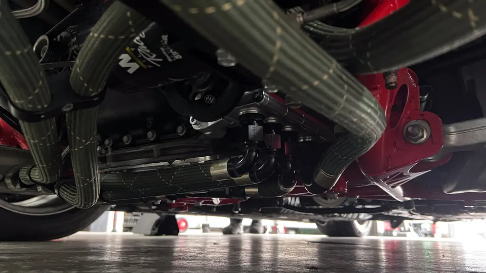 Close-up of a performance car's undercarriage showing braided oil lines, AN fittings, and an aftermarket oil filter.