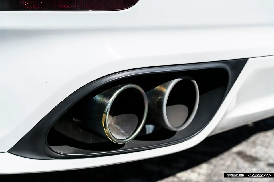 Close-up of dual performance exhaust tips on a white sports car's rear bumper, showcasing the polished finish.