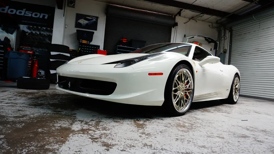 White Ferrari 458 Italia with custom chrome wheels parked inside a performance tuning shop.