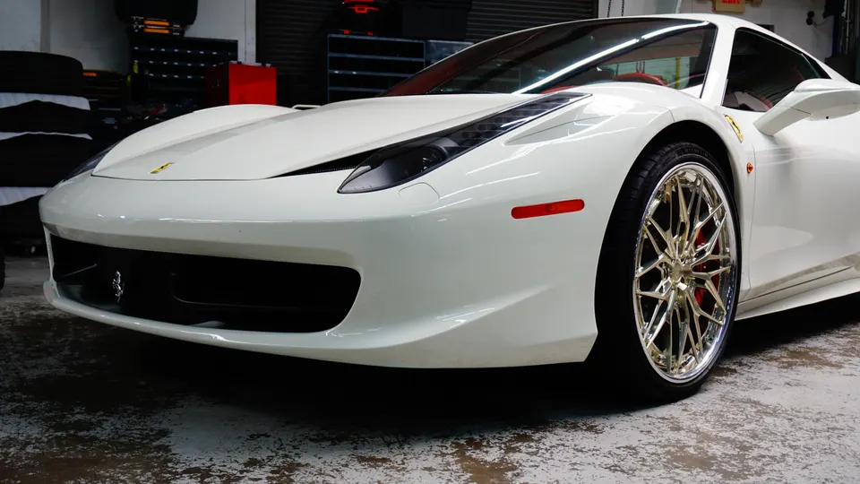 White Ferrari 458 with custom chrome wheels and red brake calipers parked in a garage.