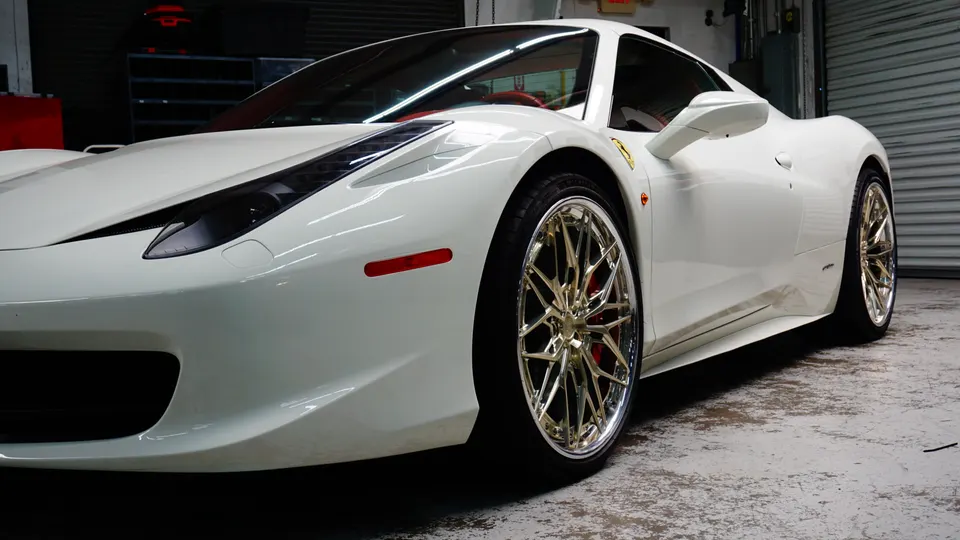 A white Ferrari sports car with custom gold multi-spoke wheels and red brake calipers parked in a garage.
