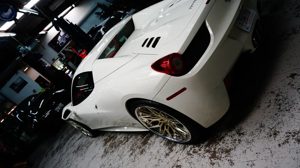 A white Ferrari 458 with gold wheels parked in a car shop, viewed from the rear quarter angle.