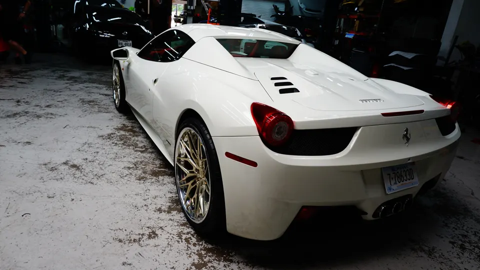 White Ferrari 458 Italia with custom gold multi-spoke wheels parked in a dimly lit garage.