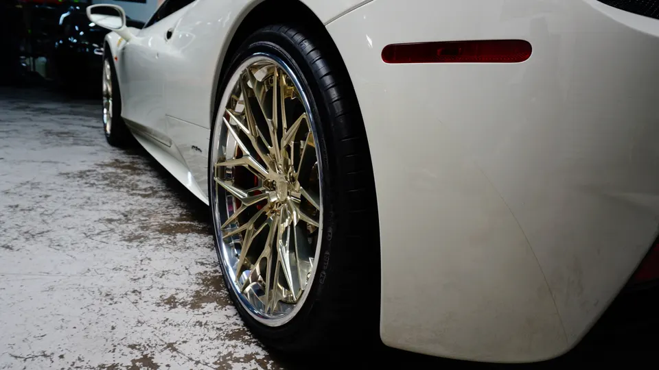 A white Ferrari with custom gold multi-spoke wheels and red brake calipers, viewed from the rear quarter.