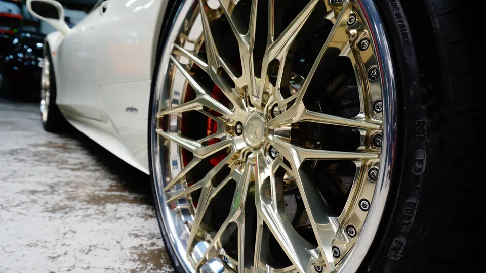 A close-up of a white luxury car's custom gold multi-spoke wheel with red brake calipers.