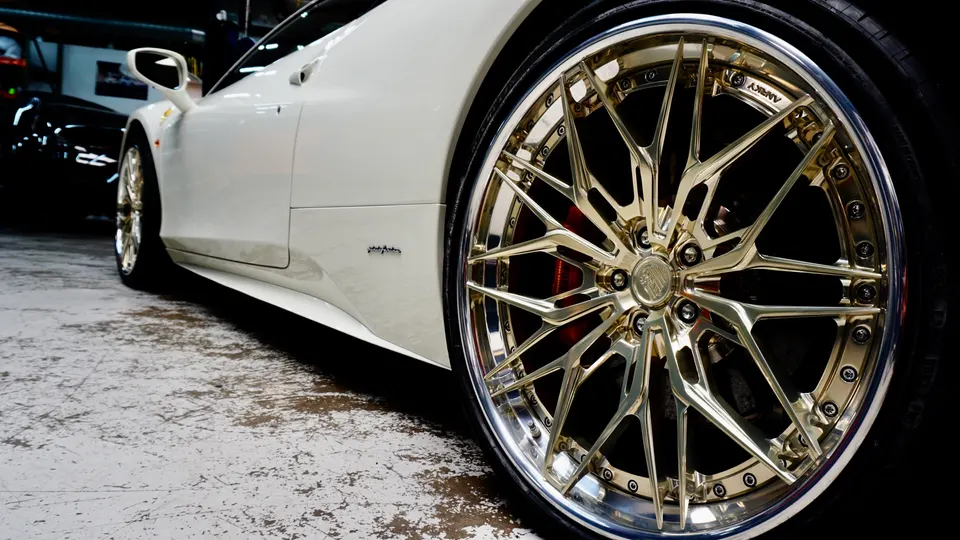 A white Ferrari with custom gold ANRKY wheels and red brake calipers in a shop setting, showcasing the wheel detail.