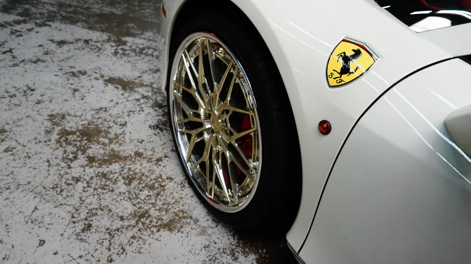 Close-up of a white Ferrari's front wheel featuring custom gold multi-spoke wheels and red brake calipers.