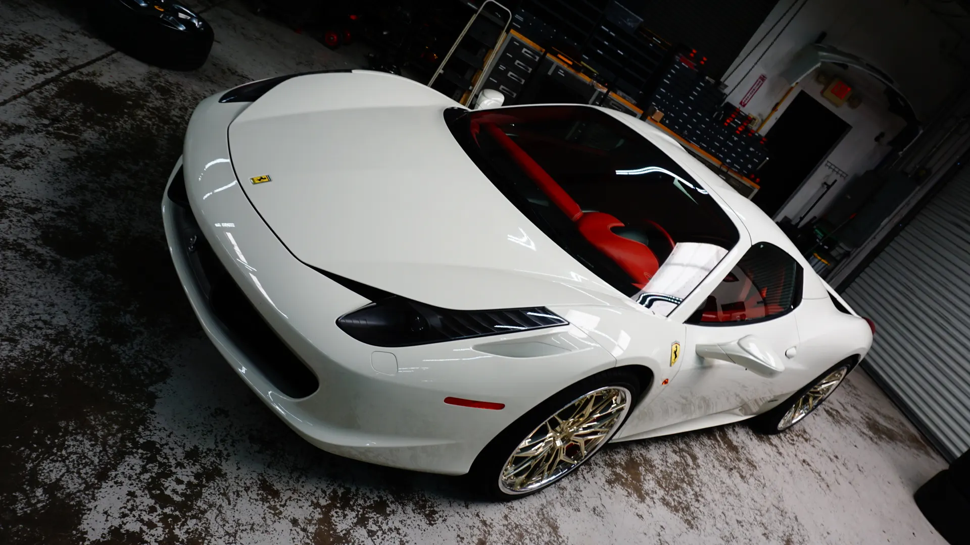 A white Ferrari 458 with custom gold wheels and red interior parked in a garage.