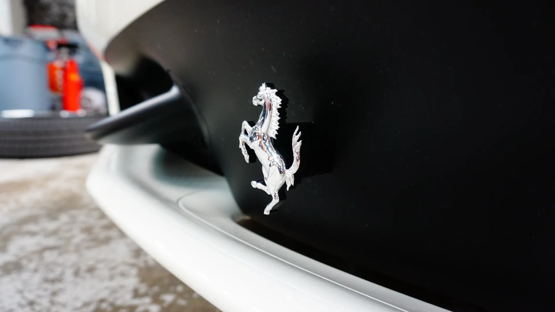 Close-up of a silver Ferrari prancing horse emblem on a black car body with a white lower trim.