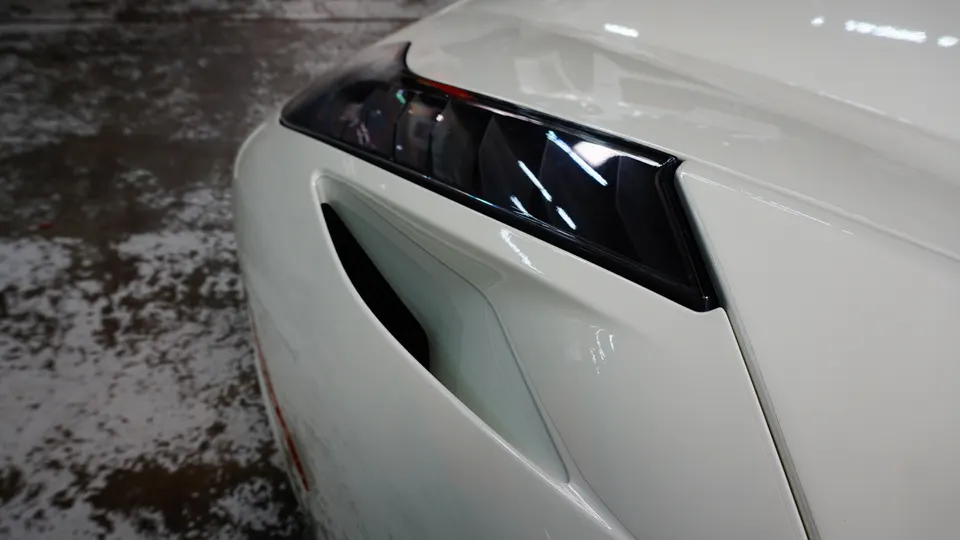 Close-up detail of the white car's front fender, headlight, and side air vent.
