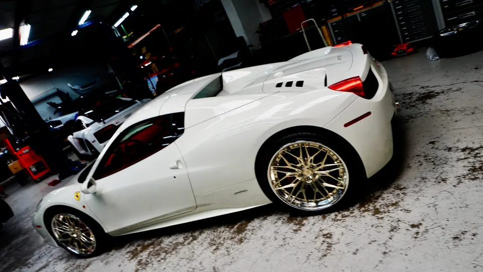 A white Ferrari 458 with custom gold wheels parked inside a performance tuning shop.
