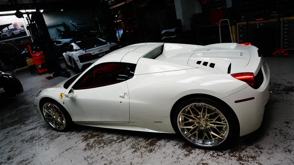White Ferrari 458 with custom gold multi-spoke wheels parked in a performance tuning shop.