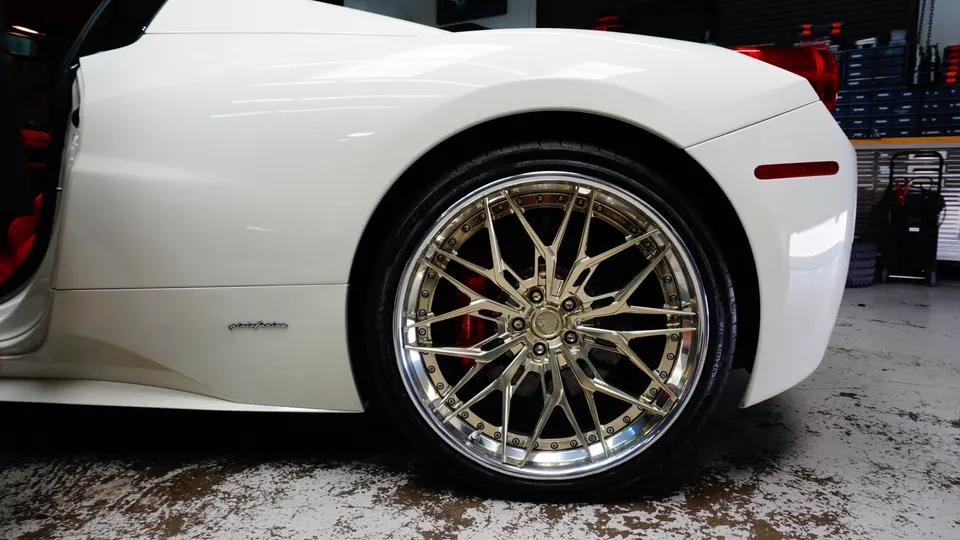 Close-up detail of a white Ferrari with custom gold multi-spoke wheels and red brake calipers.