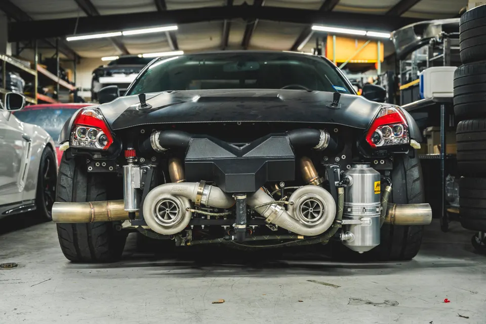 A Nissan GT-R R35 with its front bumper removed, revealing a custom twin-turbo setup in a performance shop.